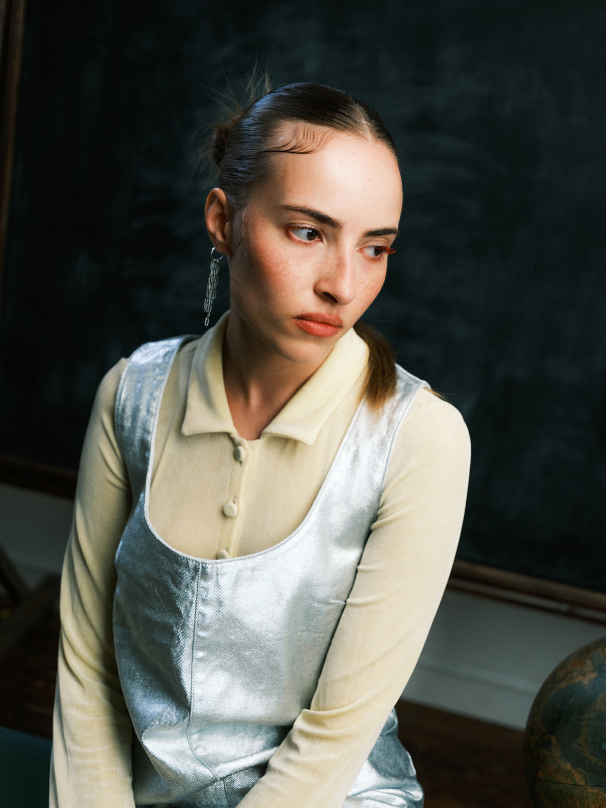 Woman in metallic dress sitting against chalkboard backdrop in classroom environment