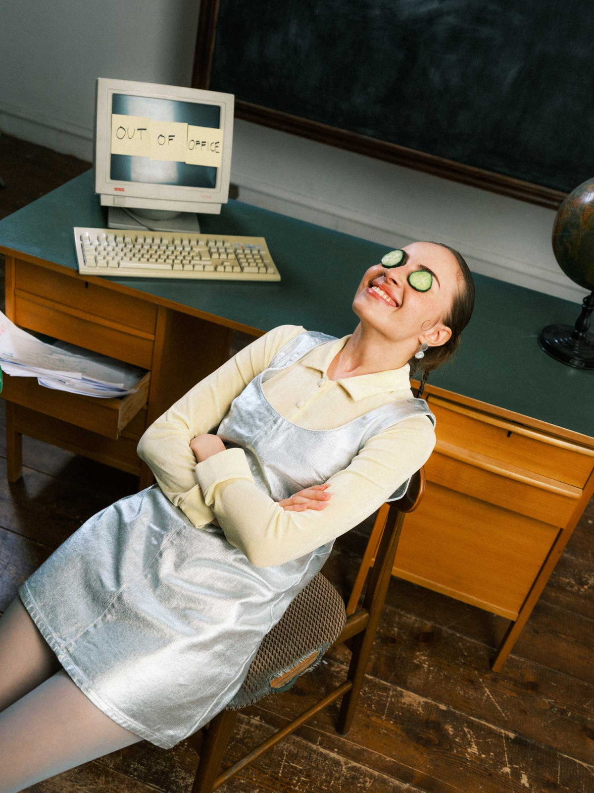 Woman in bright clothing leaning against chair with cucumber slices on her eyes in classroom environment