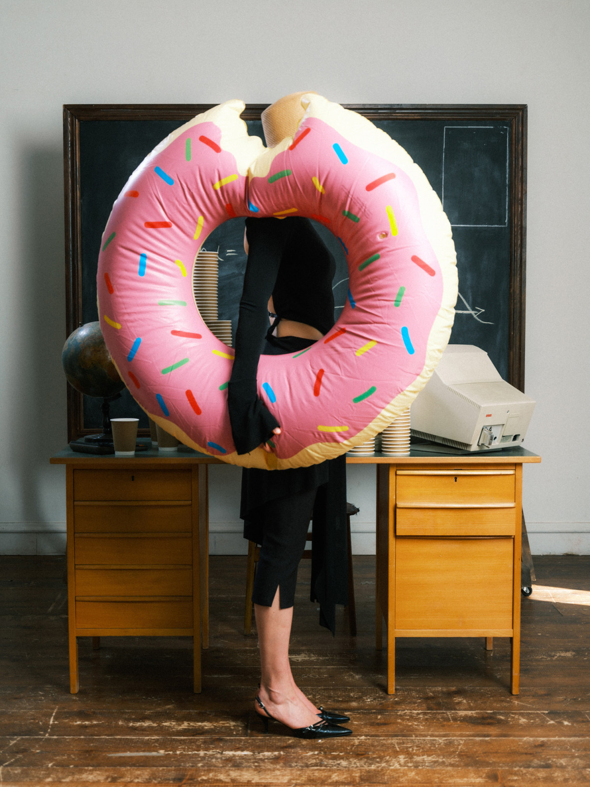 Woman in classroom environment standing in front of a vintage table holding up a doughnut shaped floatie on chalkboard backdrop